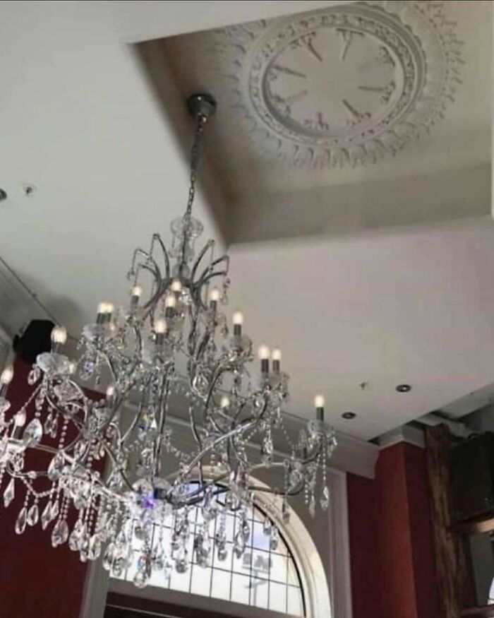 Crystal chandelier hanging off-center from decorative ceiling medallion in home design disaster with poor aesthetics.