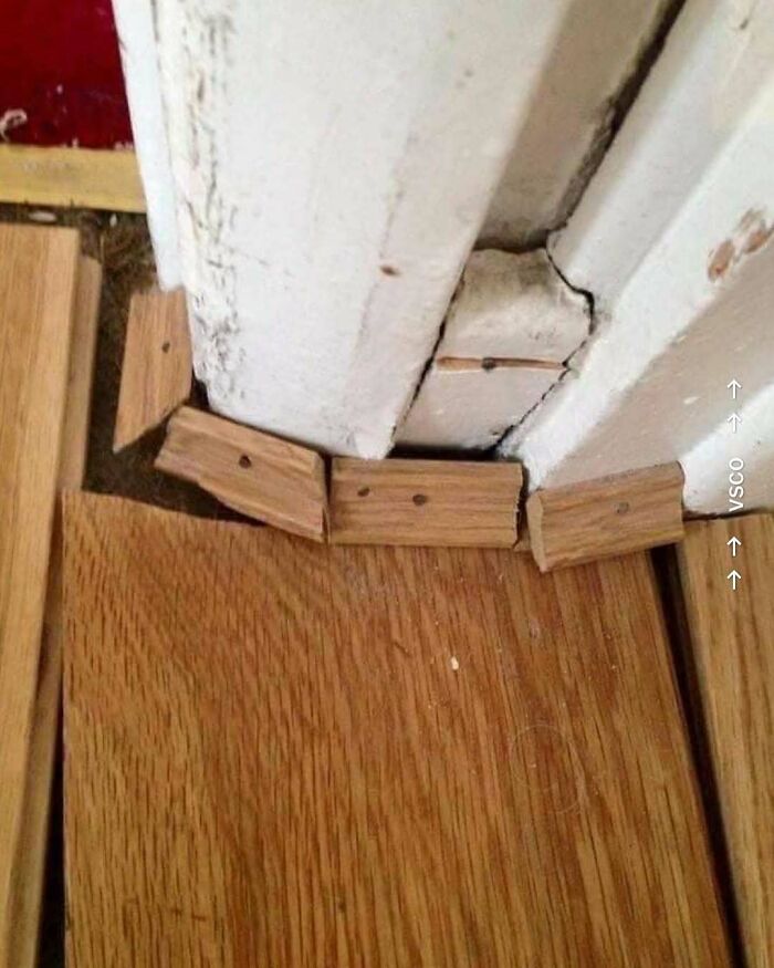 Poorly executed home design disaster with uneven wooden floor edging and mismatched trim pieces by a damaged white door frame.