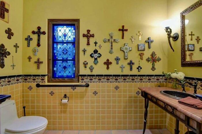 Bathroom with numerous decorative crosses on the walls, stained glass window, and mixed design elements creating a home design disaster.