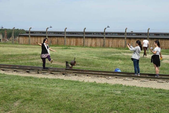 Tourists showing rude and entitled behavior while taking photos near historic train tracks in an open grassy area.