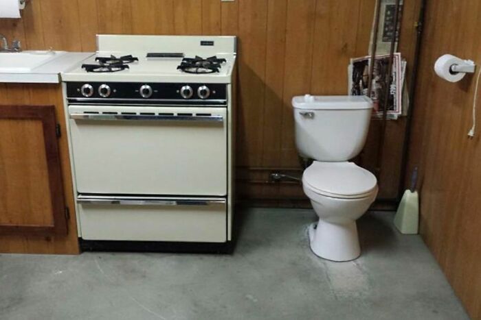 Old stove placed next to a toilet in a small room, an example of bizarre home design disasters affecting aesthetics.