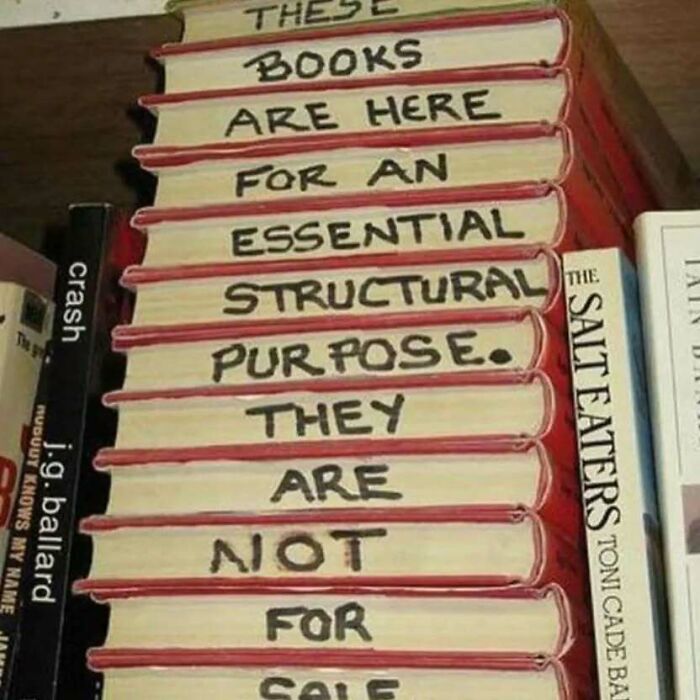 Stack of books with handwritten message about an essential structural purpose, a meme related to existential crisis.