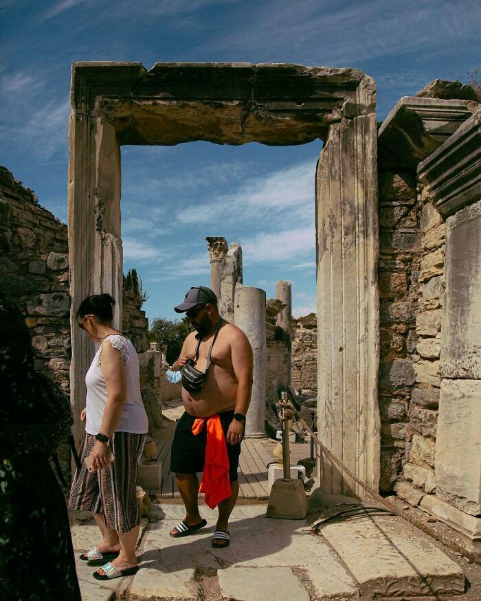 Tourists displaying entitled behavior at an ancient ruin site with stone columns and blue sky background.