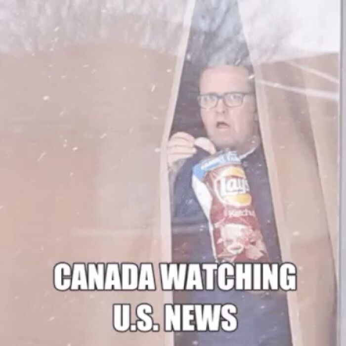 Man peeking through a curtain eating chips, representing Canada watching US news in a funny Canada meme about poutine cravings.