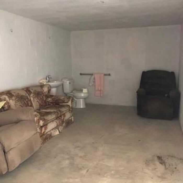 Concrete room with sofas placed next to a toilet and sink, showcasing a bizarre home design disaster with poor aesthetics.