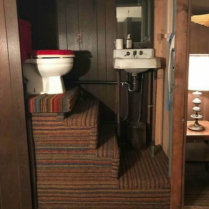 Toilet placed on carpeted stairs next to a small sink in a cramped space illustrating home design disasters and poor aesthetics.