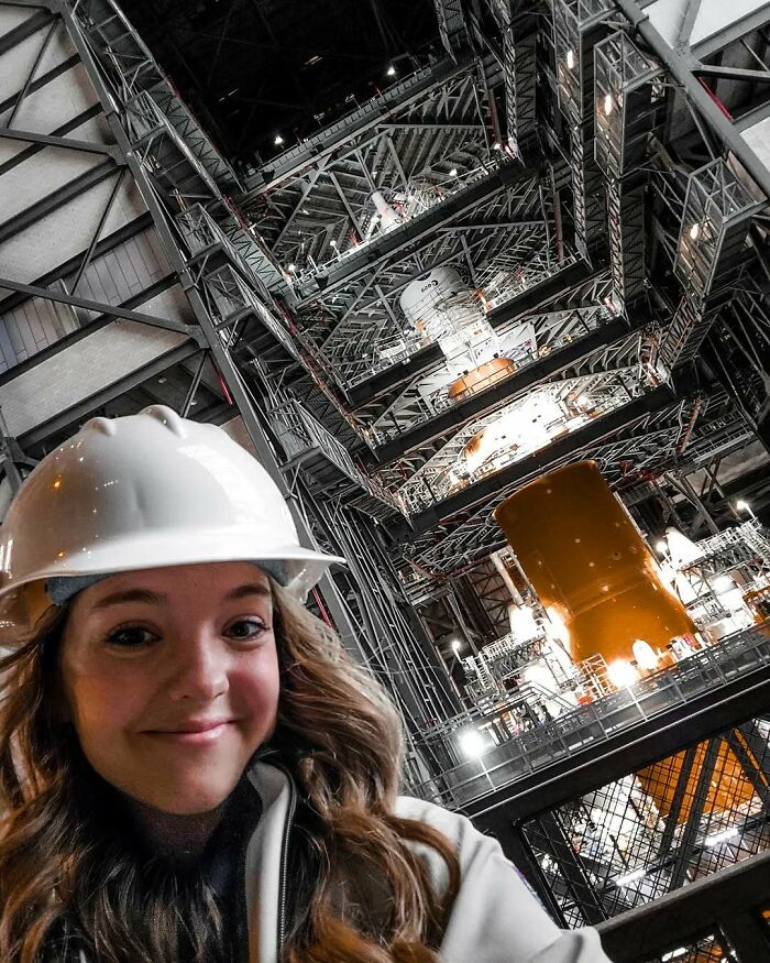 Young woman wearing a hard hat inside a large industrial structure, showcasing power tools and lab coats careers.