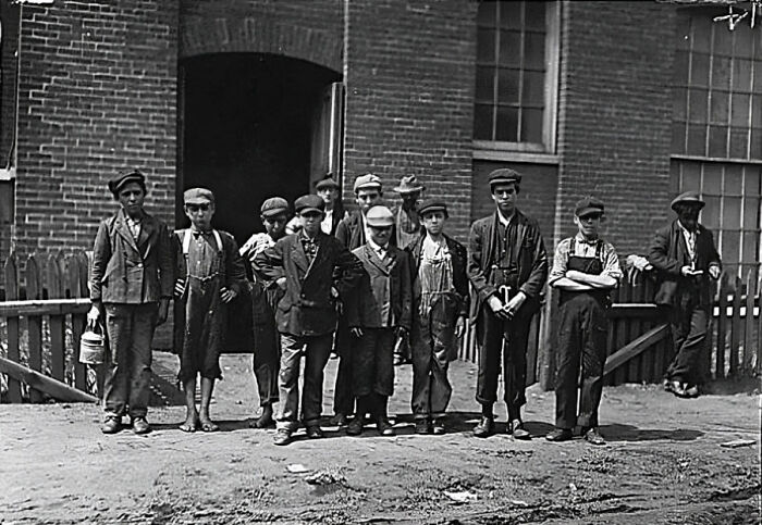 Group of boys in early 20th century clothing posing outside a brick building in a strange old photograph.