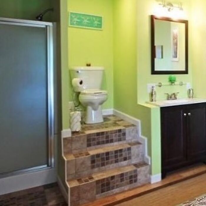 Toilet placed on tiled steps in a bathroom showcasing a home design disaster with poor functionality and aesthetics.