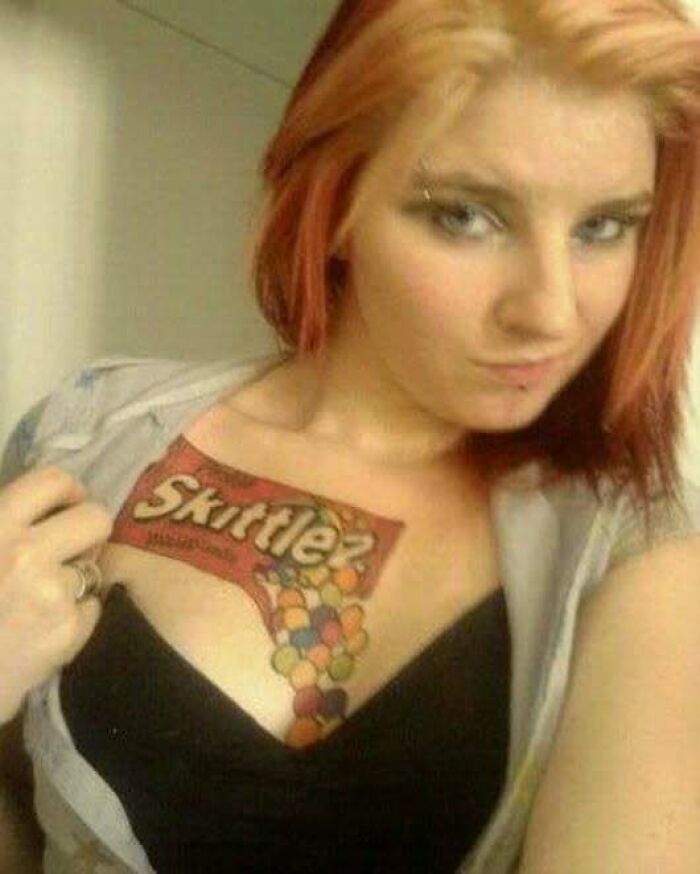Young woman revealing a large colorful Skittles tattoo on her chest, an example of ink fails and permanent regrets.