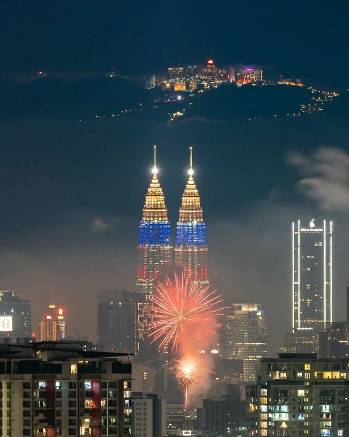 Nighttime cityscape with unedited photos featuring fireworks illuminating famous twin towers in the skyline.
