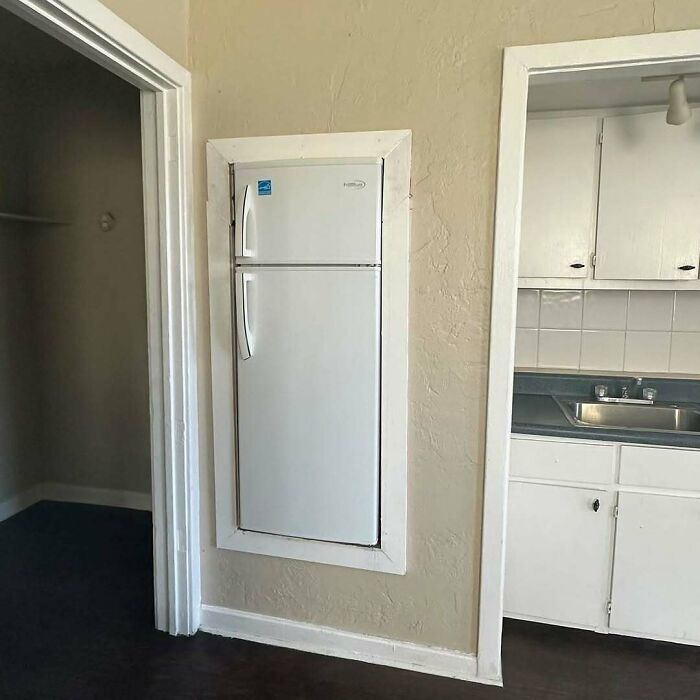 Small refrigerator oddly recessed into wall between two doorways, showcasing a home design disaster.
