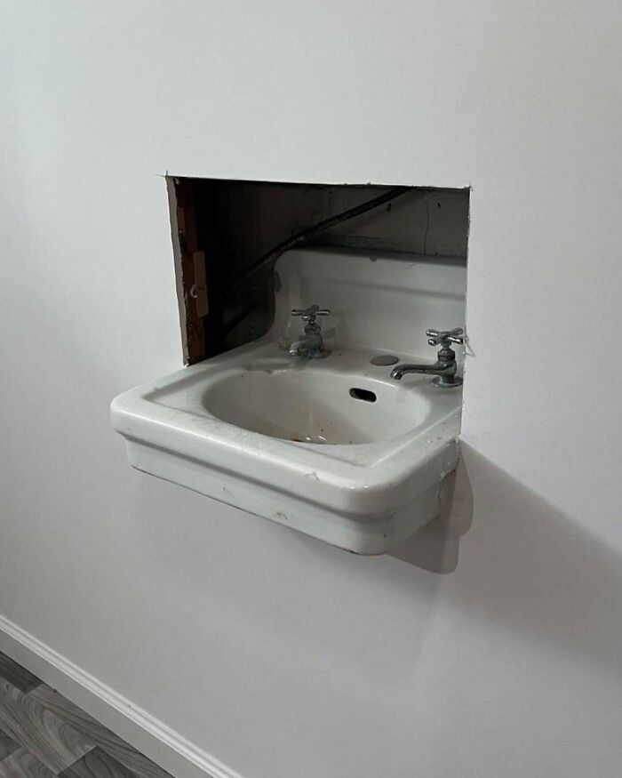 Old sink installed awkwardly inside a large hole cut unevenly in the wall showing a major home design disaster.