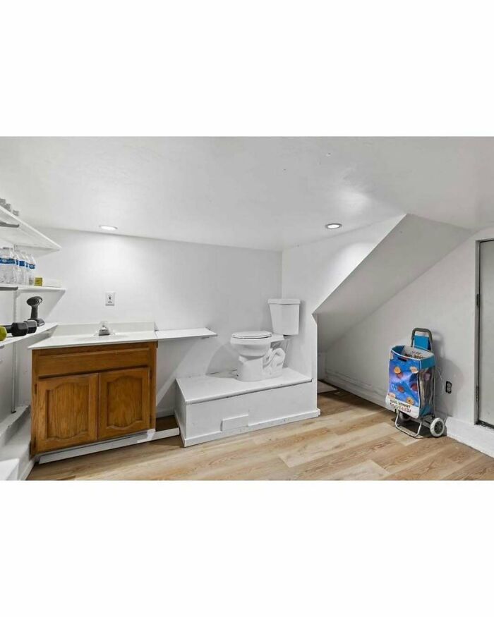 Toilet placed on a raised platform in a small room with wooden cabinet and slanted ceiling, a clear home design disaster.