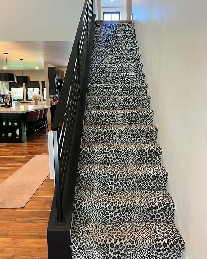 Staircase with bold leopard print carpet contrasting modern black railing and wooden floor in home design disaster.