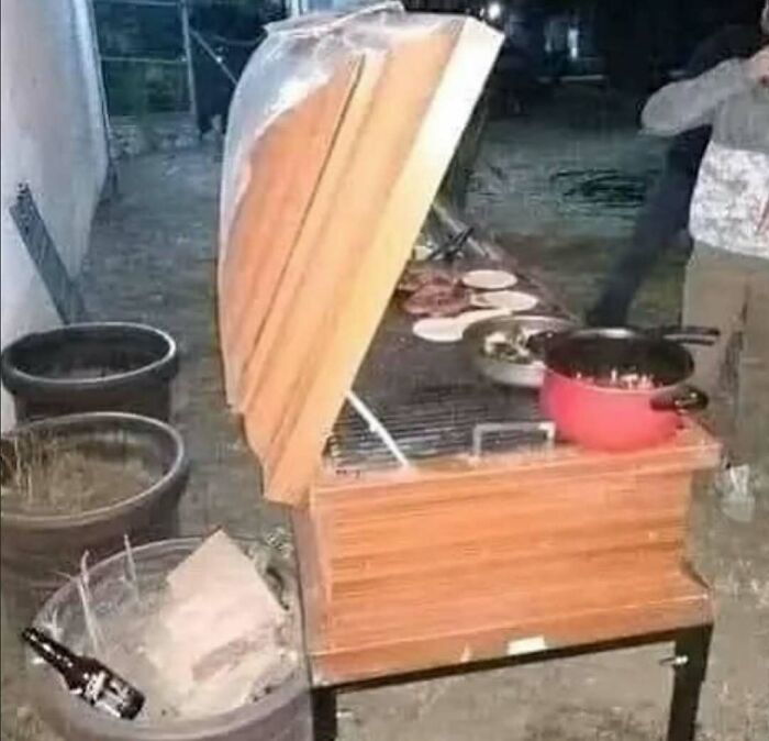 Cursed photo of a coffin repurposed as a grill with food and a pot on top in an outdoor setting at night.