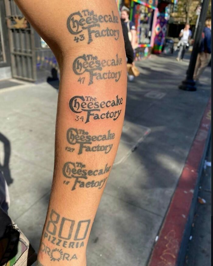 Forearm tattoo with multiple faded Cheesecake Factory logos and numbers, a cursed photo that defies logic outdoors.