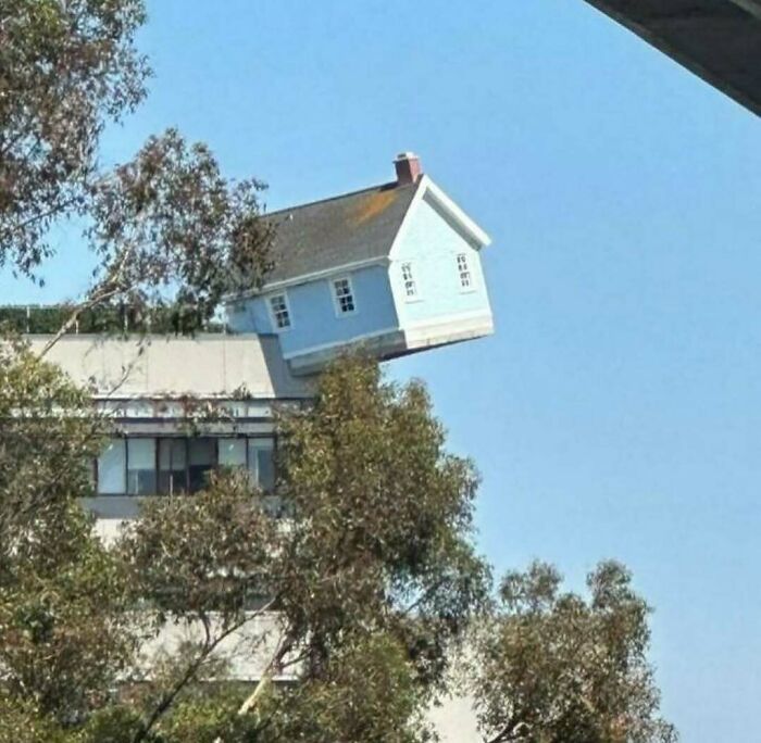 House seemingly floating and attached sideways to a building rooftop, a cursed photo that makes no sense visually.