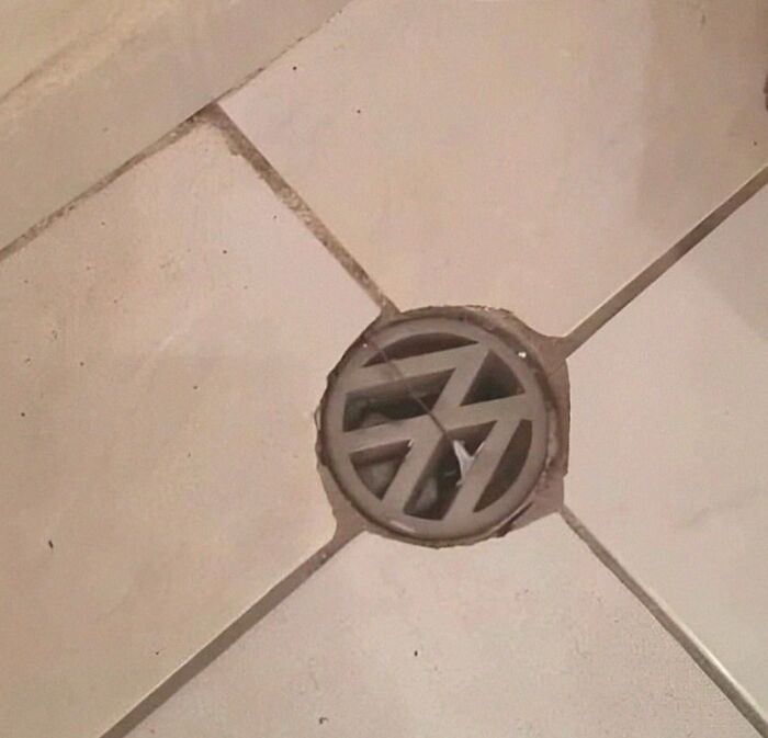 Drain cover with unusual geometric design blending into floor tiles in a cursed photo that defies logic and sense.