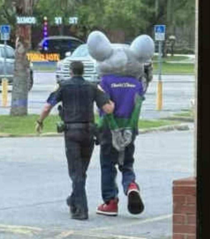 Police officer escorting a person in a large mouse costume, a cursed photo that makes absolutely zero sense.