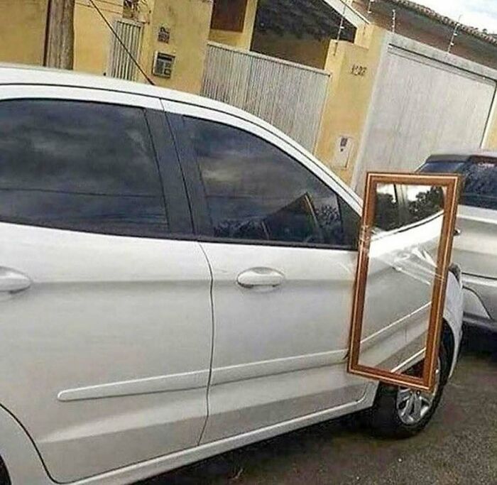 White car with a large framed mirror attached to the side, creating a confusing and cursed photo effect.