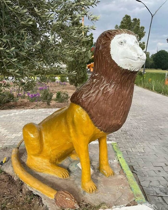 Statue of a lion with a distorted face and mismatched features in a park, a cursed photo that confuses viewers.
