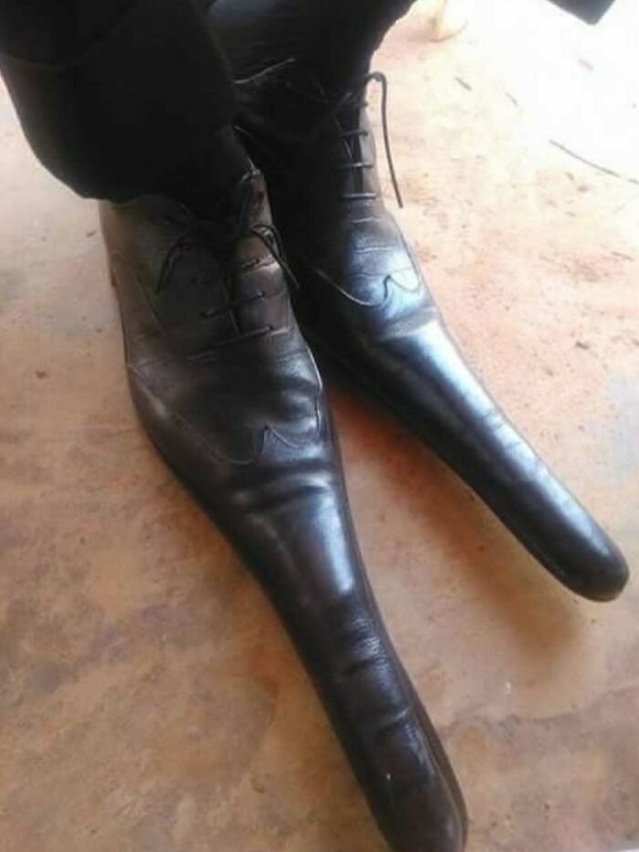 Black leather shoes with unnaturally long pointed toes creating a cursed photo that makes absolutely zero sense.
