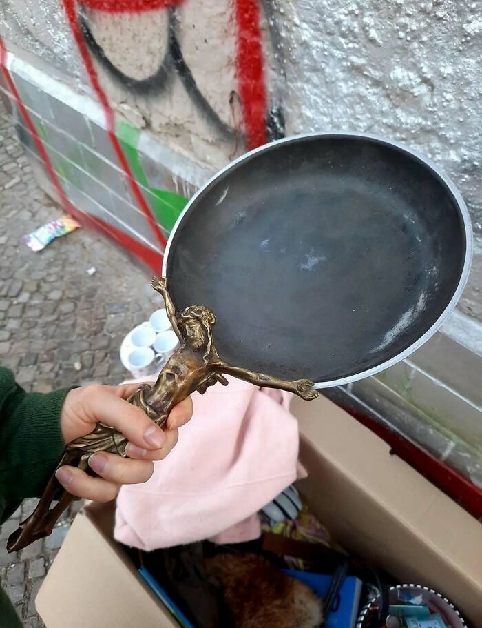 Hand holding a frying pan with a crucifix-shaped handle, one of the cursed photos that make absolutely zero sense.