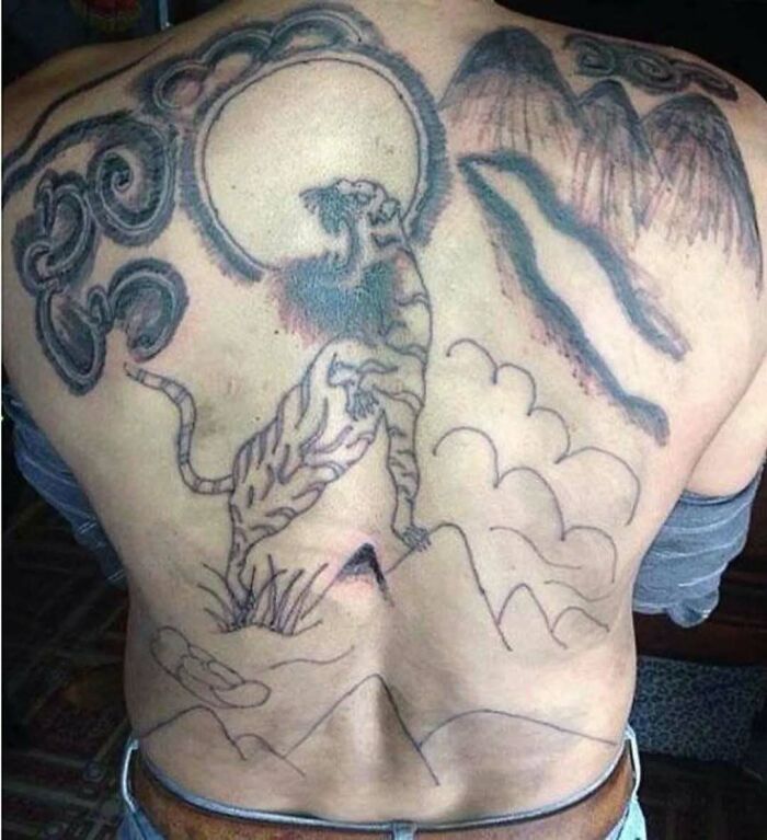 Faded and poorly executed back tattoo of a tiger and mountains showcasing ink fails and bad tattoo ideas.