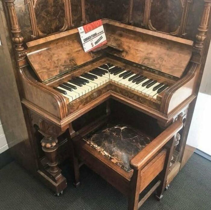 Corner piano with oddly arranged keys and worn wooden bench, a cursed photo that makes absolutely zero sense.