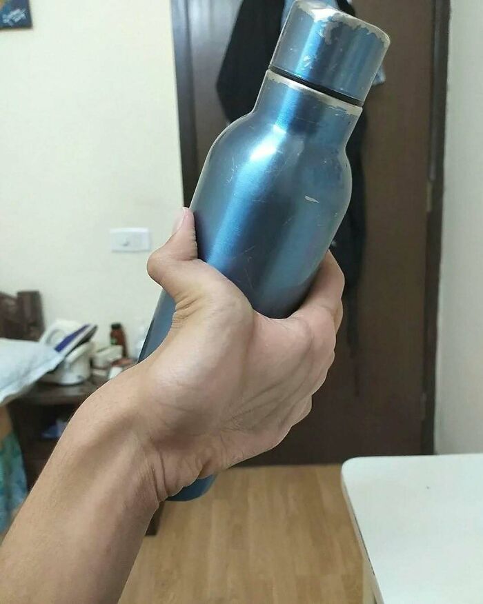 Hand holding a metallic bottle in a room, unrelated to green hairy tongue medical images or conditions.