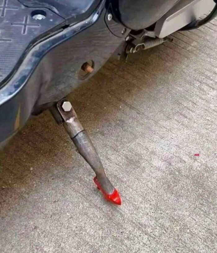 Kickstand of a motorcycle shaped like a human leg wearing a red high-heeled shoe, a cursed photo making zero sense.