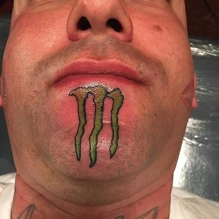 Close-up of a face tattoo fail showing a distorted Monster logo on the chin, an example of ink regrets and bad ideas.