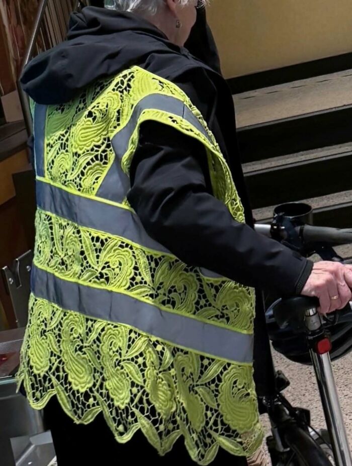 Older person wearing a high-visibility vest made of yellow lace patterns, creating a cursed photos effect that makes zero sense.