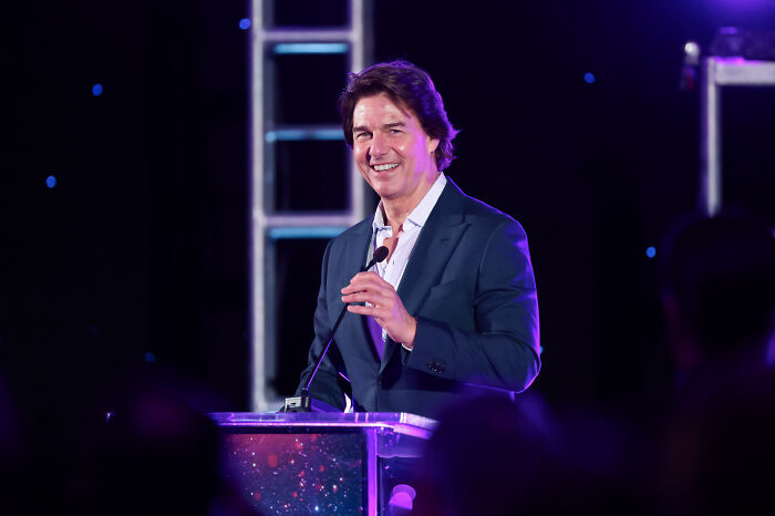Tom Cruise smiling at a podium during an event with fans speculating about Invincible Season 4 involvement.