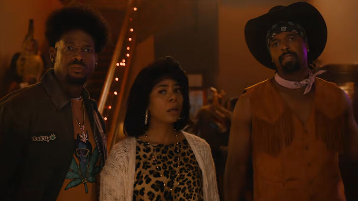 Three people in 70s-inspired outfits looking shocked in a scene from the Scary Movie 6 trailer spoofing a horror hit.
