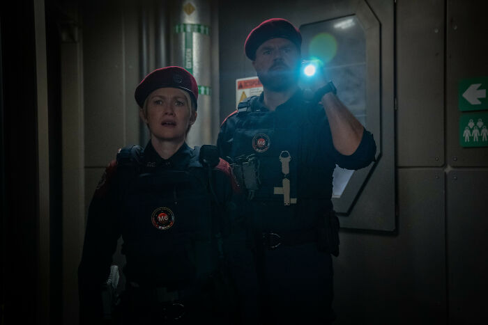 Two security officers in tactical gear and red berets exploring a dark corridor with flashlight, For All Mankind Season 5.
