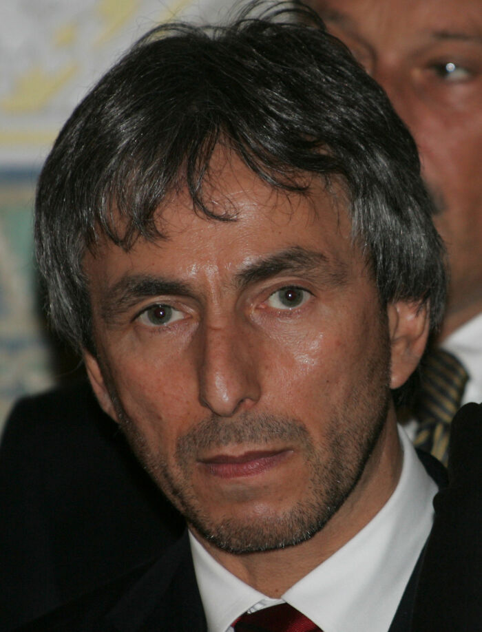 Politician linked to Ghislaine Maxwell and Epstein files, appearing serious in a formal suit and tie close-up portrait.