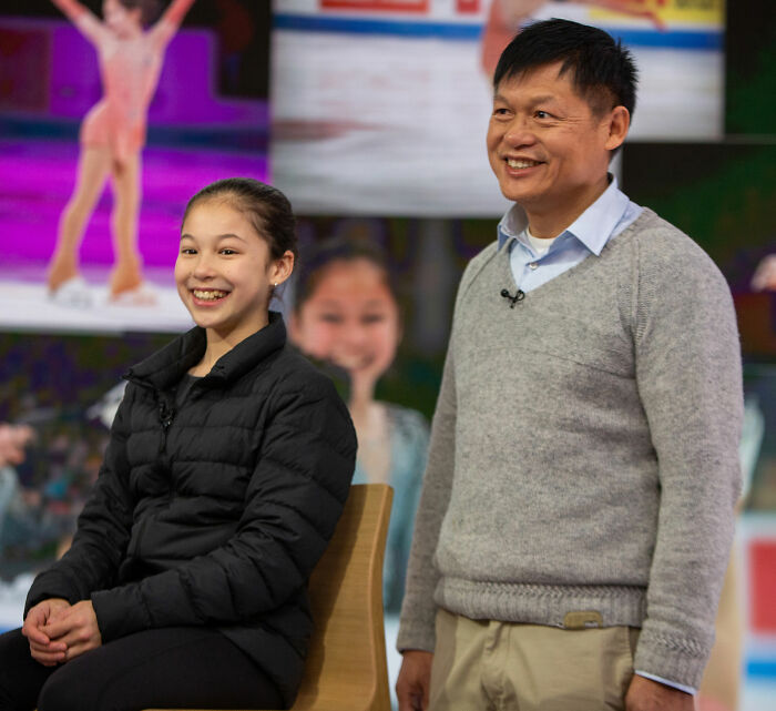 Alysa Liu smiling seated next to a man, during an interview discussing her childhood and World Championships withdrawal.