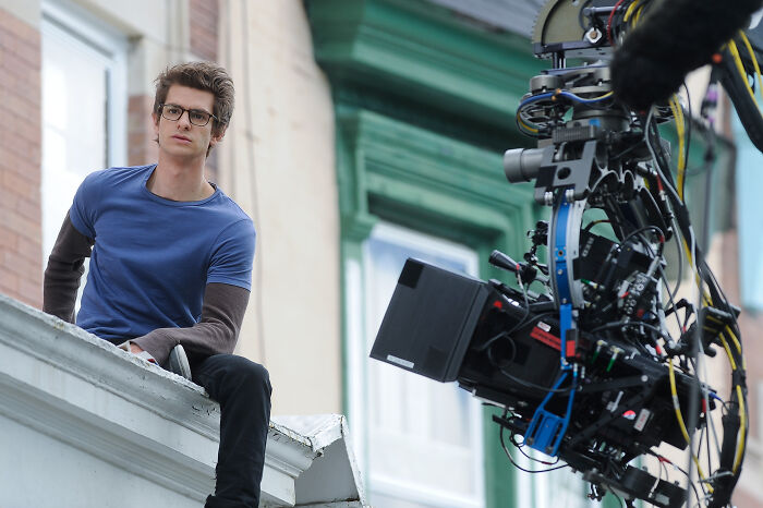 Andrew Garfield on set wearing glasses and casual clothes while filming, highlighting Harry Potter artists' work.