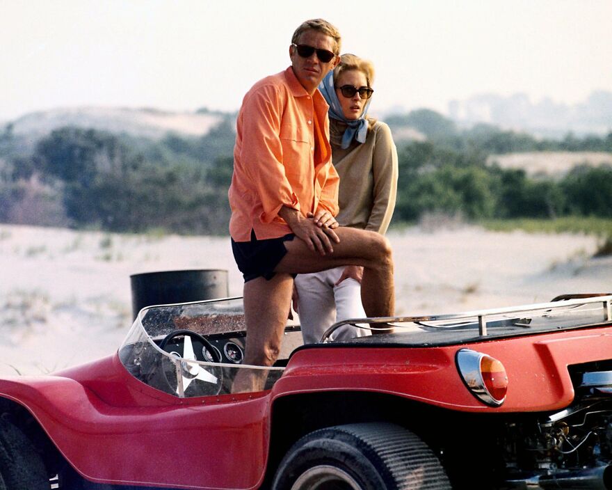 Man and woman wearing sunglasses beside a red vintage car at the beach representing Michael B Jordan movie themes.