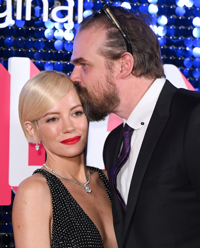 David Harbour’s alleged partner in a close moment with a woman at a formal event with a blue and white backdrop.