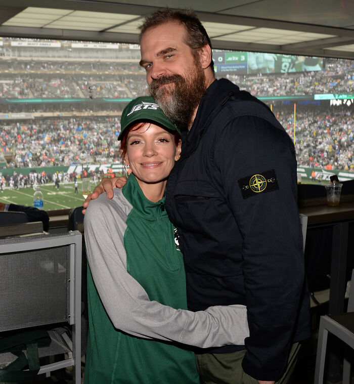 David Harbour’s alleged partner and another person posing together at a crowded sports event stadium.