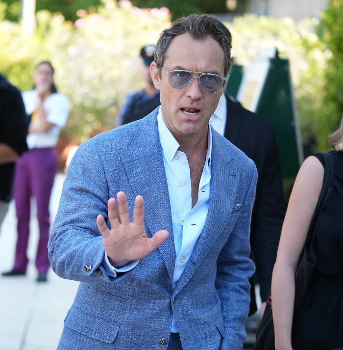 Homem de terno azul e óculos escuros levantando a mão, relacionado a Chappell Roan banido do festival por questão de segurança.