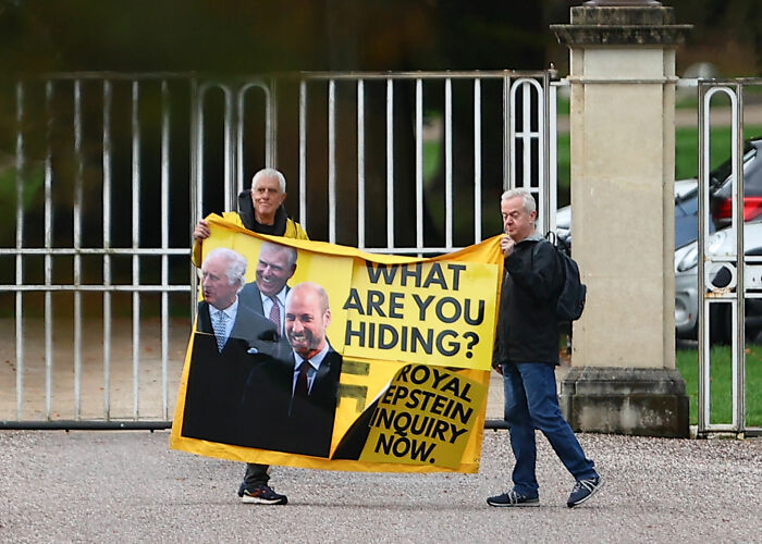 Two men holding a protest banner about royal inquiry, referencing Prince William and a royal family gathering.