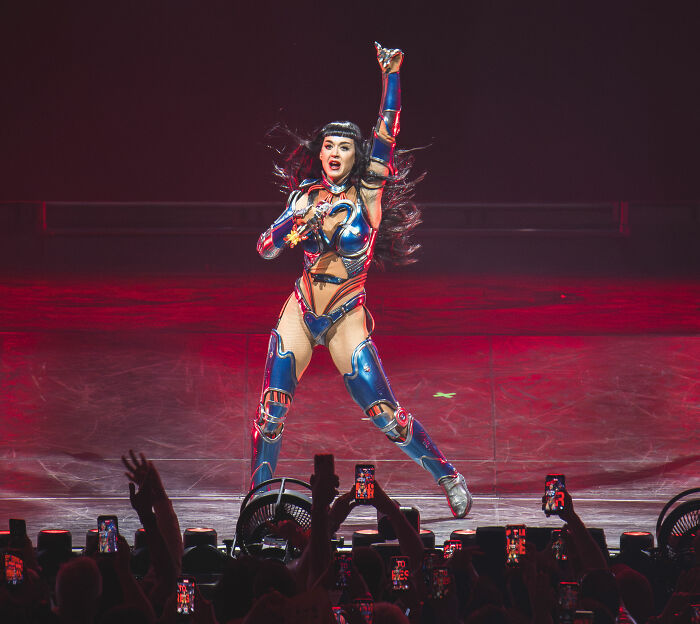 Katy Perry performing in a futuristic outfit on stage with fans capturing the moment during a live concert.