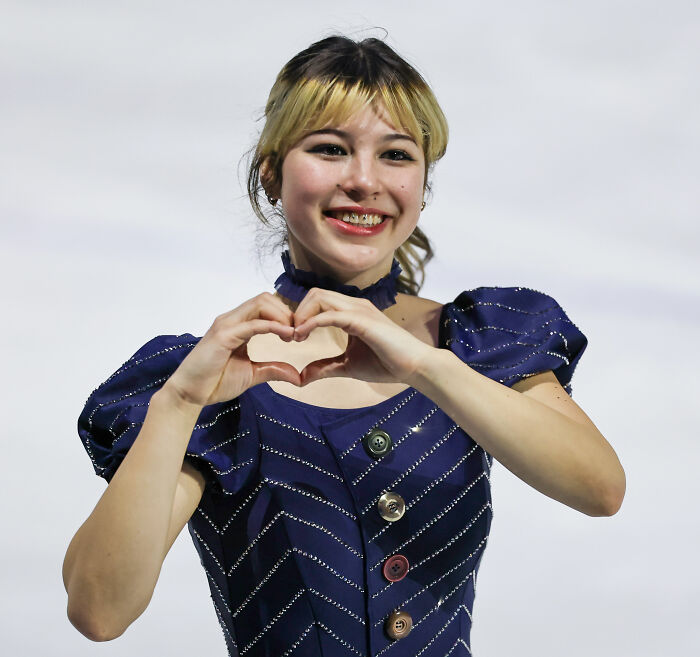 Alysa Liu smiling and forming a heart with her hands wearing a navy blue outfit after a world championship event.