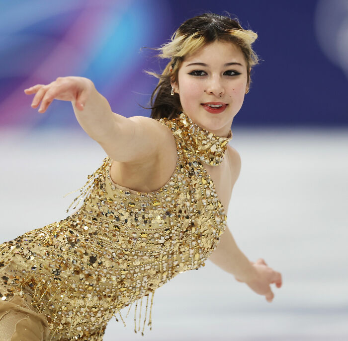 Figure skater Alysa Liu performing on ice in a sparkling gold costume showing strength and focus in her Olympic routine.