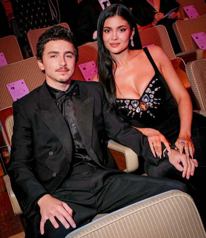 Timoth&eacute;e Chalamet and date seated together at an awards event, dressed in elegant evening attire.