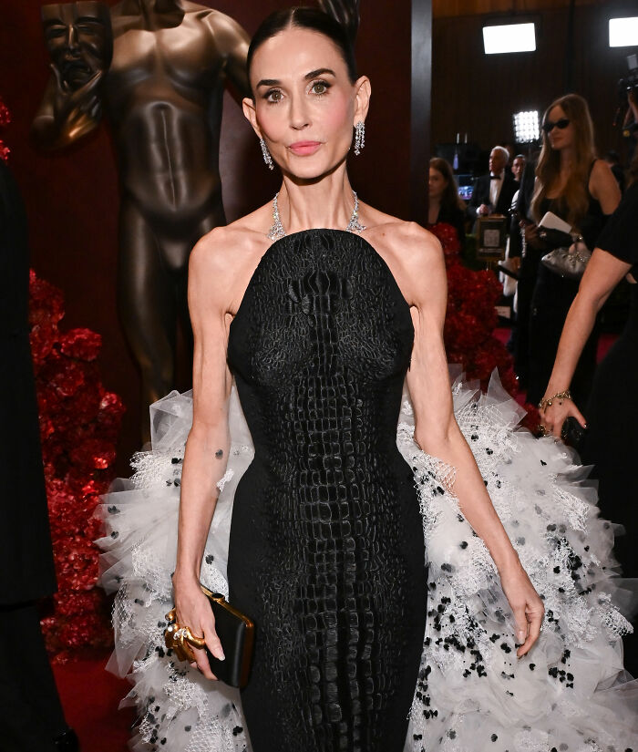 Demi Moore on the red carpet in a black textured gown, showcasing her beauty transformation and sparking beauty standard debate.